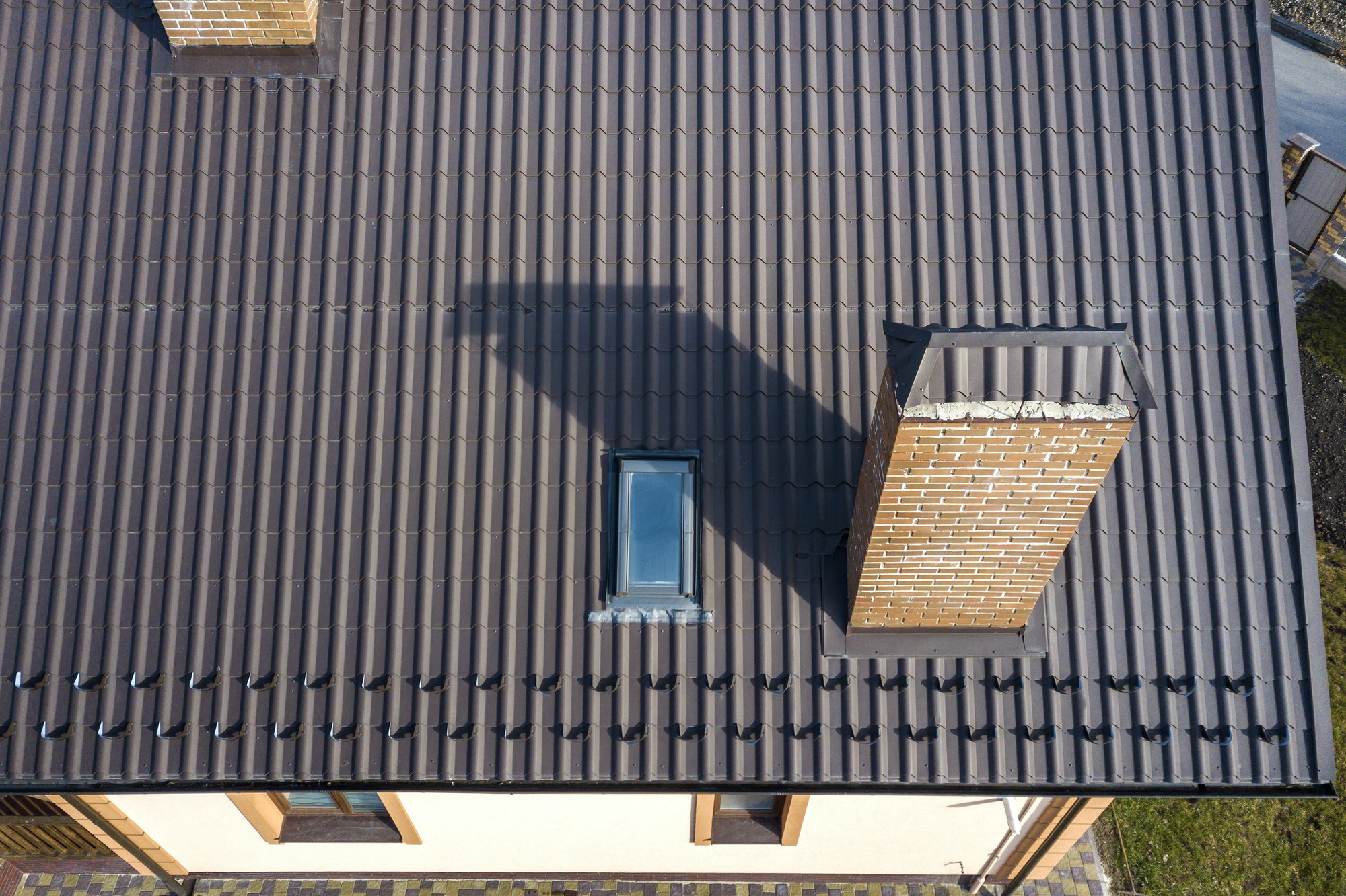 Aerial top view of building steep shingle roof, brick chimneys and small attic window on house top