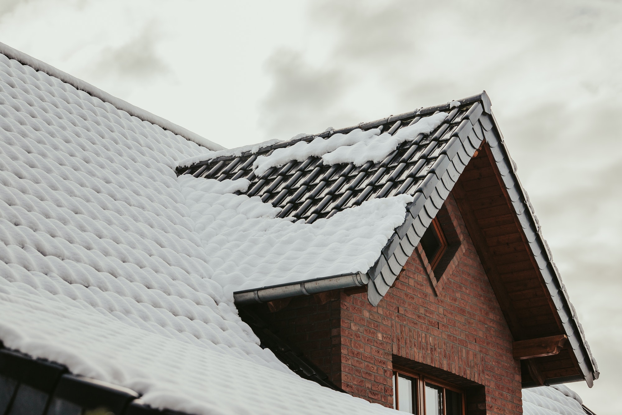 Low angle shot of a roof of a brick building covered in the snow under a cloudy sky